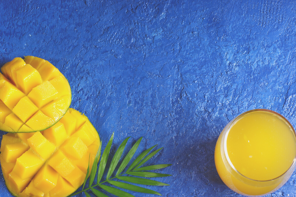 Creative layout on a blue background with mango, a glass of juice and a palm leaf.